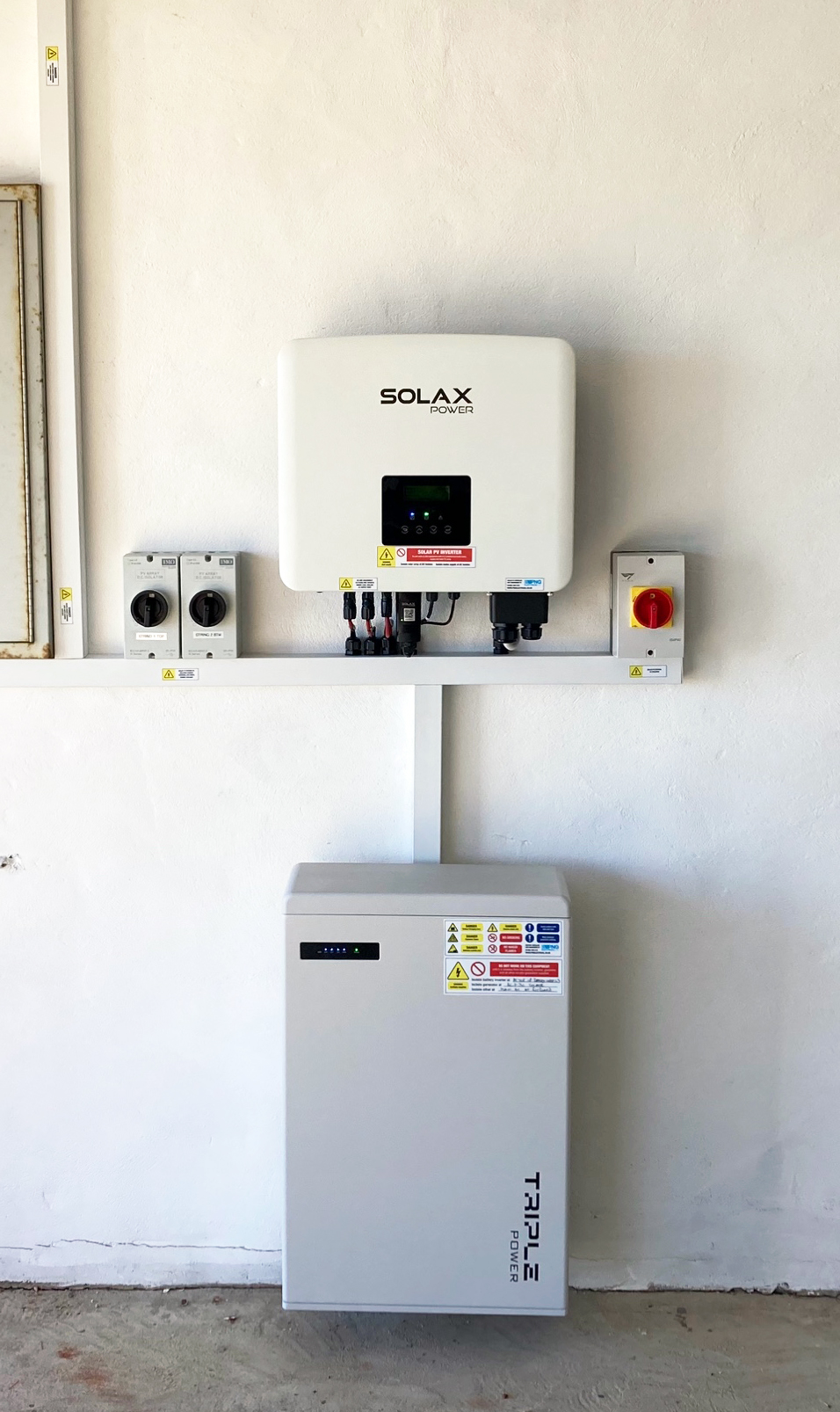 Wall-mounted SOLAX inverter and Triple Power battery storage unit with electrical switches, installed on a white wall.
