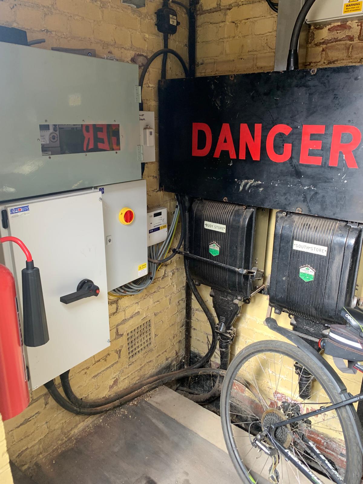 Electrical panels and equipment labelled “DANGER” mounted on a brick wall, with a bicycle partially visible in the lower right corner.