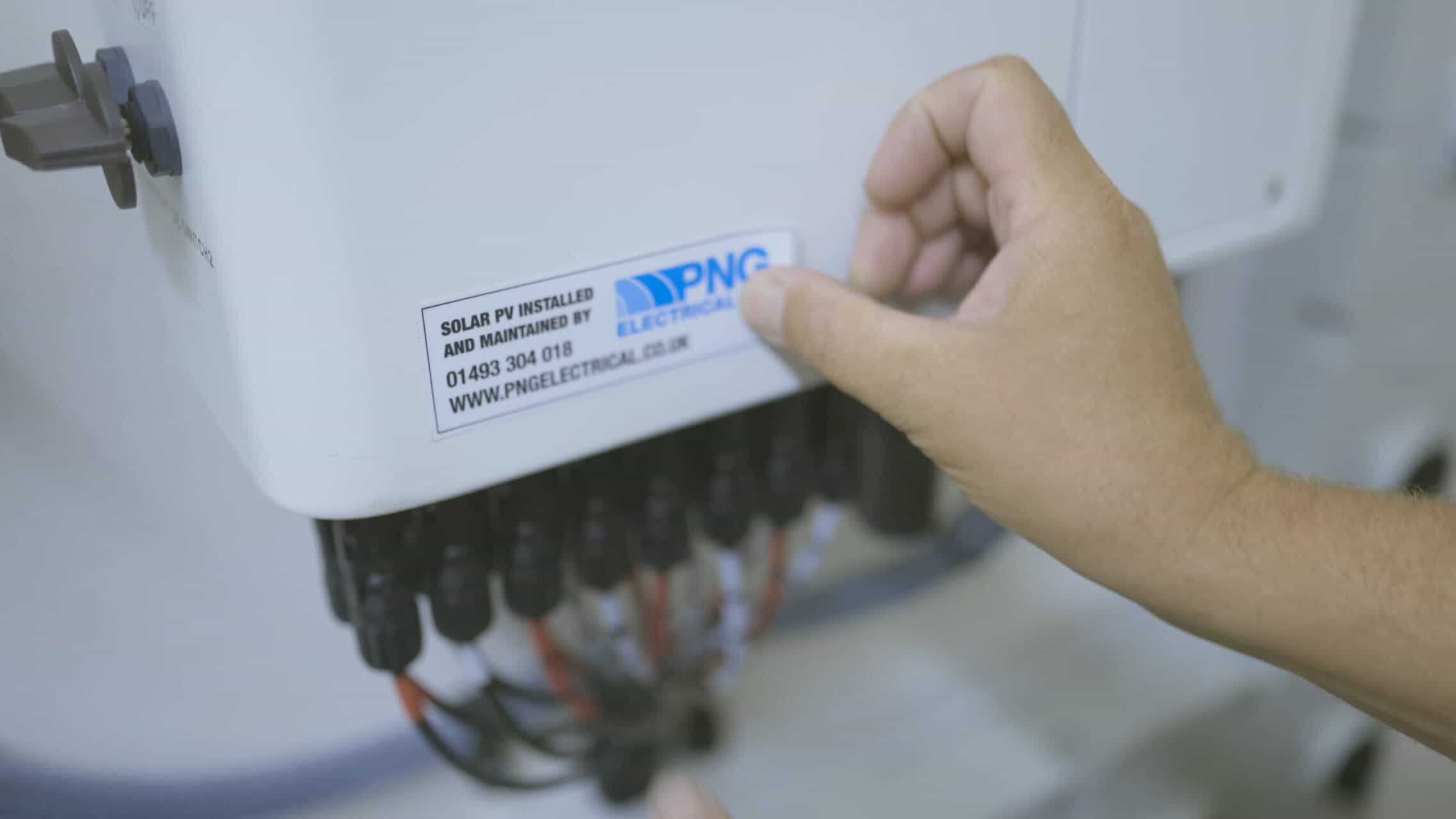 A hand is placing or touching a PNG Electrical sticker on a white electrical box with multiple black cables connected at the bottom.