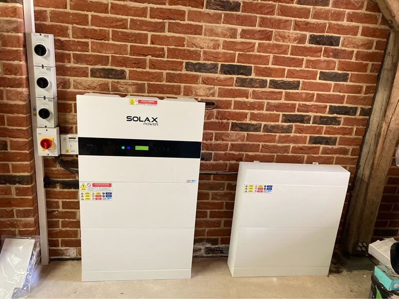 A Solax Power inverter and battery unit are mounted against a brick wall, with electrical switches visible to the left.
