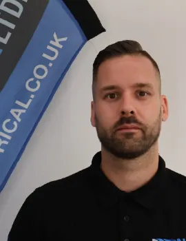 A man with a beard wearing a black polo shirt, standing in front of a blue banner with partial text reading “CAL.CO.UK”.